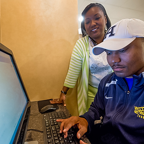 Woman stands behind man while he types at a computer